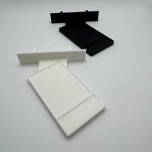 Puede incluir: Dos soportes de estanter&iacute;a de pl&aacute;stico, uno blanco y otro negro. Ambos soportes tienen forma rectangular con un peque&ntilde;o labio en la parte superior y dos peque&ntilde;os agujeros en la parte inferior.