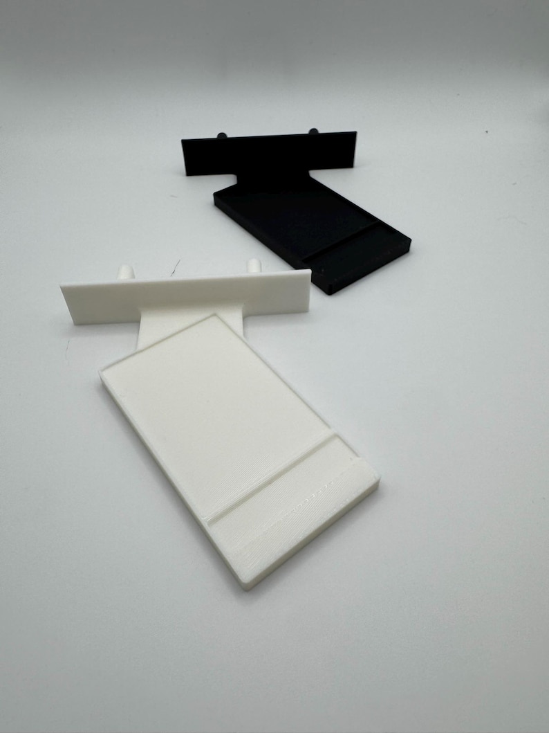Puede incluir: Dos soportes de estanter&iacute;a de pl&aacute;stico, uno blanco y otro negro. Ambos soportes tienen forma rectangular con un peque&ntilde;o labio en la parte superior y dos peque&ntilde;os agujeros en la parte inferior.