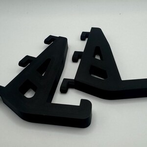May include: Two black plastic shelf brackets, each with a triangular shape and multiple holes for mounting.