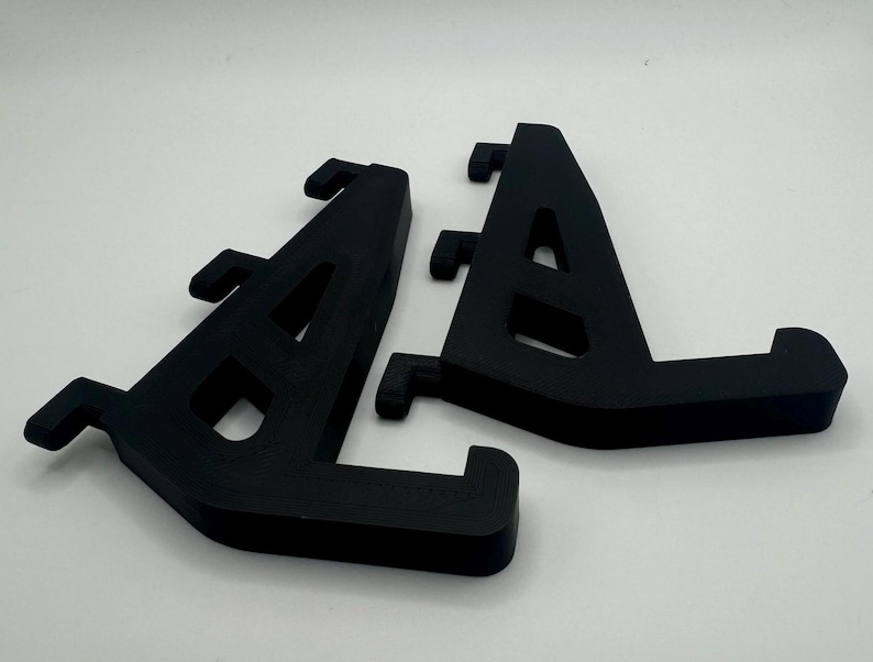 May include: Two black plastic shelf brackets, each with a triangular shape and multiple holes for mounting.