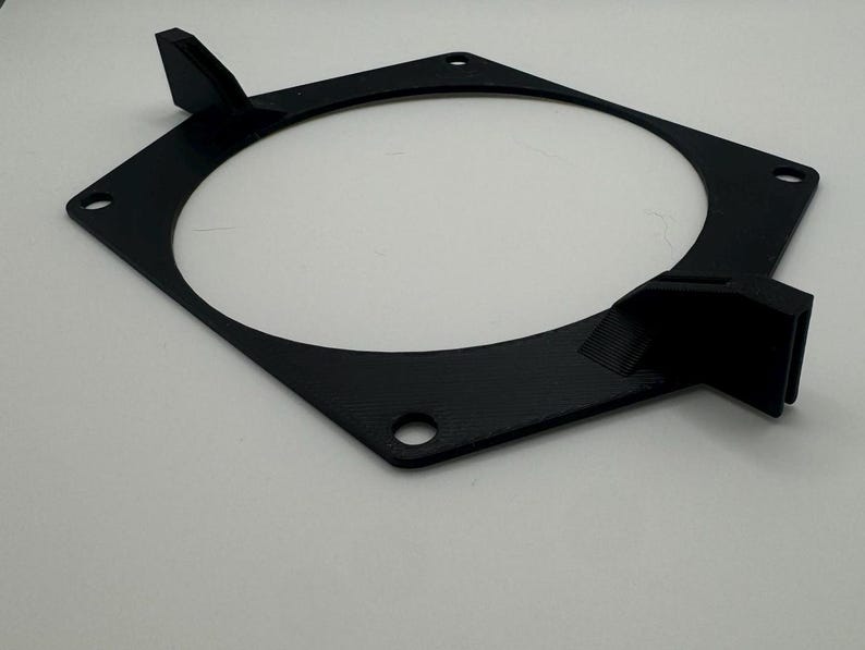 以下が含まれることがあります： 黒色のプラスチック製のファンマウント。側面にタブが2つ、ネジ穴が4つあります。