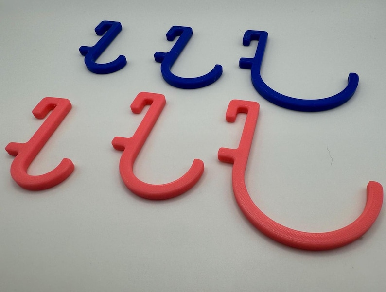 Puede incluir: Cinco ganchos impresos en 3D, dos son rosas y tres son azules. Los ganchos tienen todos la misma forma, pero los ganchos rosas son ligeramente m&aacute;s peque&ntilde;os que los ganchos azules.
