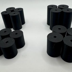 May include: A set of 18 black rubber cylindrical spacers with a hole in the center. The spacers are arranged in three groups of six.