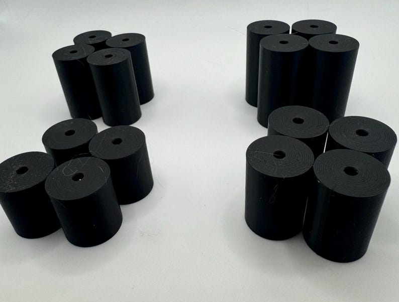 May include: A set of 18 black rubber cylindrical spacers with a hole in the center. The spacers are arranged in three groups of six.