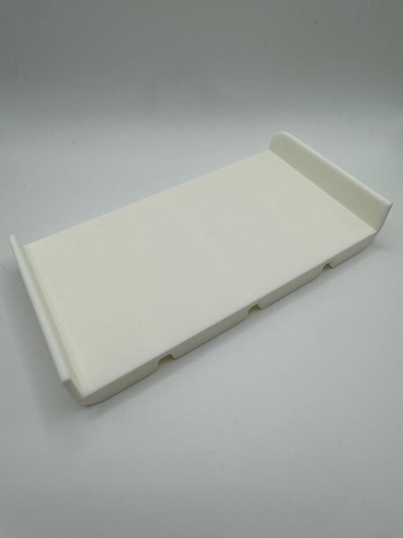 May include: A white plastic tray with three small holes on the bottom. The tray has rounded edges and a smooth surface.
