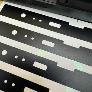May include: Four black sticker sheets with cutouts for buttons, a small rectangle, and three small circles. The stickers are on a white background.