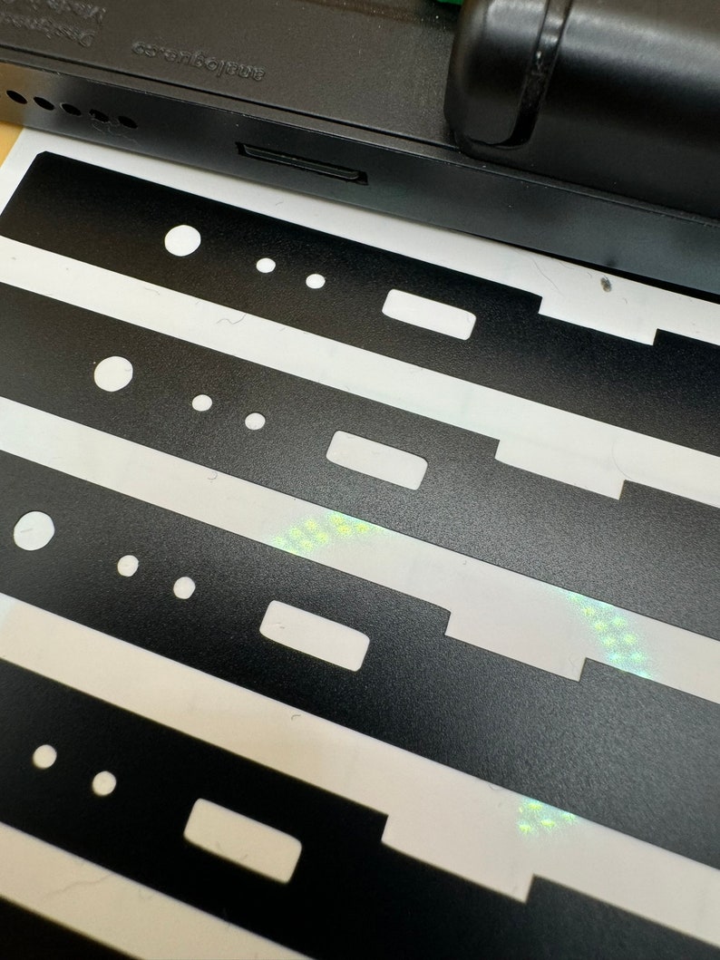 May include: Four black sticker sheets with cutouts for buttons, a small rectangle, and three small circles. The stickers are on a white background.