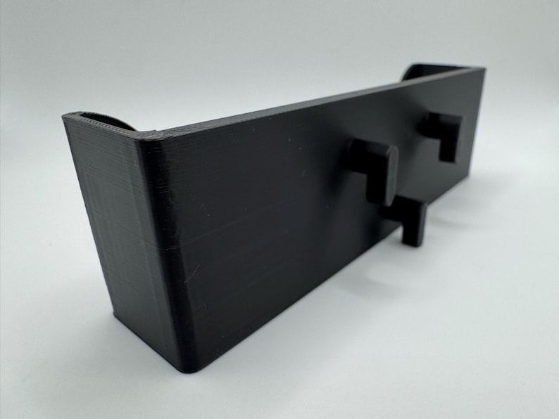Op de afbeelding: Zwarte plastic wandbevestiging met twee kleine rechthoekige knoppen.