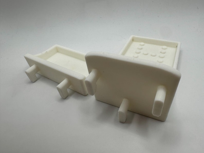 May include: Two off-white ceramic trays with rectangular bases and raised edges. Each tray has four short, rectangular legs. One tray has a series of small, rounded indentations on its surface.