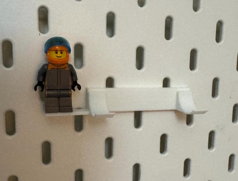 May include: A white plastic pegboard shelf with a blue and yellow Lego minifigure standing on it.