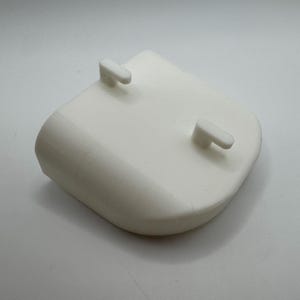 K&ouml;nnte beinhalten: Ein wei&szlig;es Kunststoffbauteil mit abgerundeter Form und zwei kleinen, rechteckigen Vorspr&uuml;ngen. Das Objekt hat eine glatte, matte Oberfl&auml;che und ist wahrscheinlich Teil einer gr&ouml;&szlig;eren Baugruppe. Das Design ist einfach und funktional.