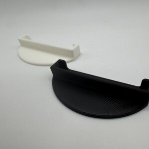 May include: Two half-circle shaped objects. One is white, the other is black. Both have a handle-like extension. The objects appear to be made of plastic. The black object has a textured surface.
