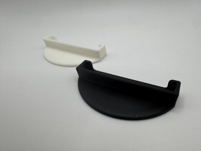 May include: Two half-circle shaped objects. One is white, the other is black. Both have a handle-like extension. The objects appear to be made of plastic. The black object has a textured surface.