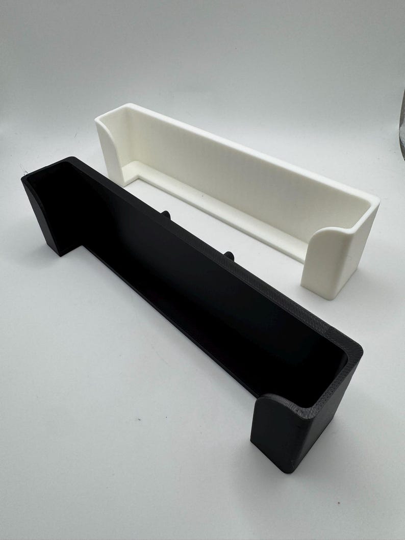 May include: Two rectangular storage containers, one black and one white, are displayed. Each container has a long, open top and raised sides. The black container is in the foreground, with the white container slightly behind it.