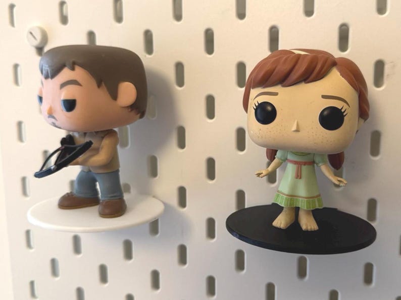 Op de afbeelding: Twee Funko Pop-figuren op displayschappen. De figuur links is een mannelijke figuur met bruin haar en een bruin en zwarte outfit. De figuur rechts is een vrouwelijke figuur met rood haar en een groene jurk.
