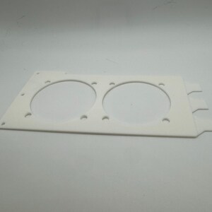 Peut inclure: Plaque en plastique blanc avec deux d&eacute;coupes circulaires pour ventilateurs. La plaque comporte plusieurs petits trous autour des bords et trois languettes sur le c&ocirc;t&eacute; droit.