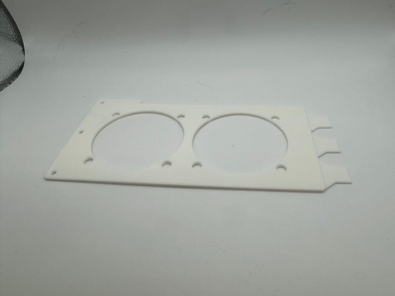 Peut inclure: Plaque en plastique blanc avec deux d&eacute;coupes circulaires pour ventilateurs. La plaque comporte plusieurs petits trous autour des bords et trois languettes sur le c&ocirc;t&eacute; droit.