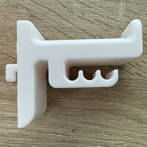 Pu&ograve; includere: Un supporto da parete bianco stampato in 3D con un design unico. Presenta una barra orizzontale con tre fessure curve e una sezione verticale con una piccola sporgenza. Il supporto &egrave; progettato per il montaggio a parete.
