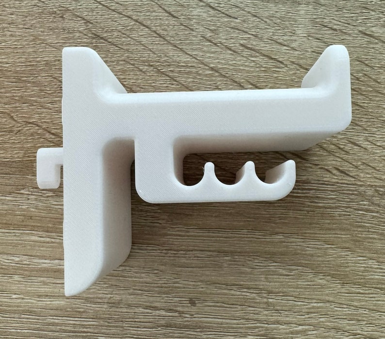 Pu&ograve; includere: Un supporto da parete bianco stampato in 3D con un design unico. Presenta una barra orizzontale con tre fessure curve e una sezione verticale con una piccola sporgenza. Il supporto &egrave; progettato per il montaggio a parete.