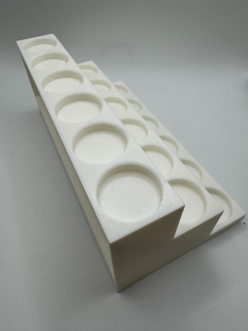Puede incluir: Un soporte blanco escalonado para botes de pintura con m&uacute;ltiples aberturas circulares. El soporte est&aacute; hecho de un material s&oacute;lido y opaco. El dise&ntilde;o est&aacute; inclinado para facilitar el acceso.