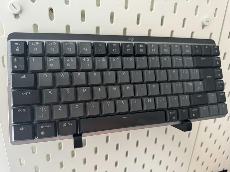 May include: A black Logitech keyboard with white lettering on the keys. The keyboard has a number pad and function keys. The keyboard is mounted on a wall.
