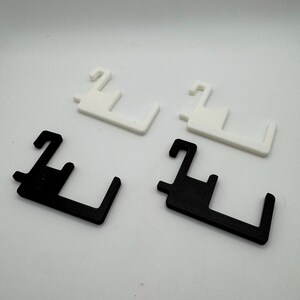 May include: Four plastic door handle helpers. Two are white, and two are black. Each has a hook-like top and a rectangular base with a curved edge. The items are arranged on a white surface.