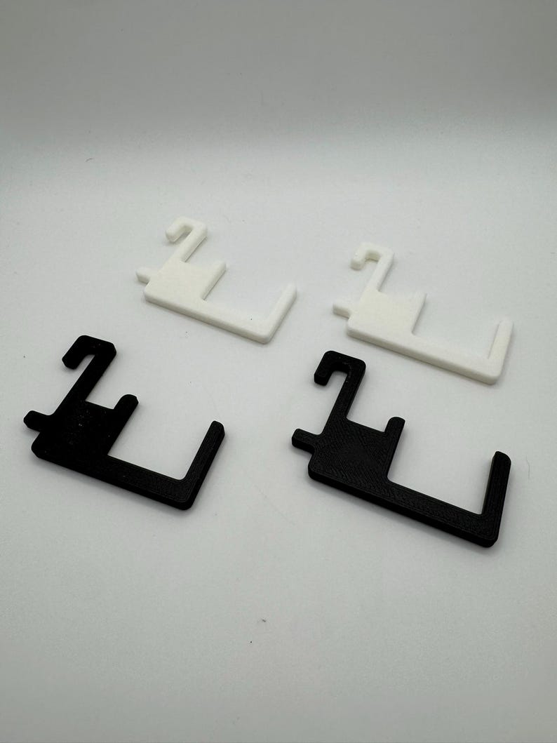 May include: Four plastic door handle helpers. Two are white, and two are black. Each has a hook-like top and a rectangular base with a curved edge. The items are arranged on a white surface.