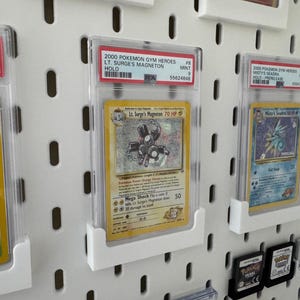 Peut inclure: Pr&eacute;sentation de cartes Pok&eacute;mon class&eacute;es, dont une carte Holo Lt. Surge's Magneton de 2000 Pok&eacute;mon Gym Heroes, expos&eacute;es dans des &eacute;tuis de protection. Les cartes sont mont&eacute;es sur un panneau perfor&eacute; blanc.