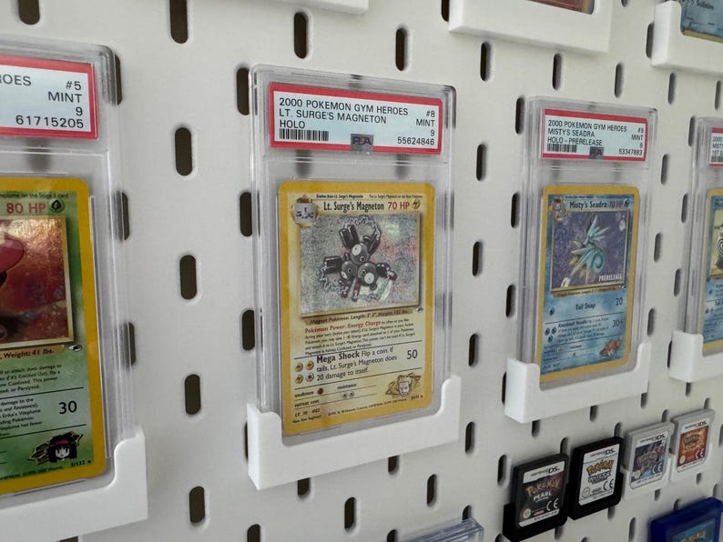 Peut inclure: Pr&eacute;sentation de cartes Pok&eacute;mon class&eacute;es, dont une carte Holo Lt. Surge's Magneton de 2000 Pok&eacute;mon Gym Heroes, expos&eacute;es dans des &eacute;tuis de protection. Les cartes sont mont&eacute;es sur un panneau perfor&eacute; blanc.