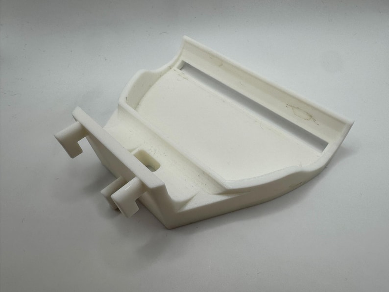 May include: A white, 3D-printed plastic object with a curved design. It features a rectangular opening and two protruding, rectangular tabs. The object appears to be a component or part of a larger assembly.