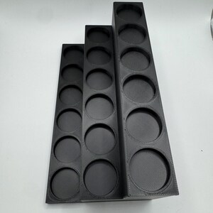 Puede incluir: Tres organizadores negros escalonados con aberturas circulares. Los organizadores son de diferentes alturas, el m&aacute;s alto tiene m&aacute;s aberturas. Los organizadores est&aacute;n hechos de un material negro mate y est&aacute;n dispuestos en una configuraci&oacute;n escalonada.