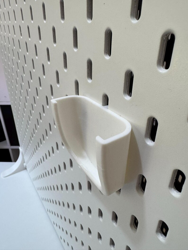 K&ouml;nnte beinhalten: Eine wei&szlig;e Lochwand mit einem befestigten wei&szlig;en Haken. Die Lochwand hat zahlreiche kleine, gleichm&auml;&szlig;ig verteilte L&ouml;cher. Der Haken ist so konzipiert, dass er in die L&ouml;cher passt und eine Aufbewahrungsl&ouml;sung bietet. Die Lochwand und der Haken bestehen aus einem soliden, langlebigen Material.