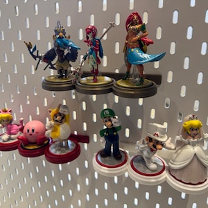 May include: A collection of colorful figurines displayed on a white pegboard. The figurines include characters from popular video games, such as Mario, Zelda, and Kirby. The figurines are displayed on small, round platforms.