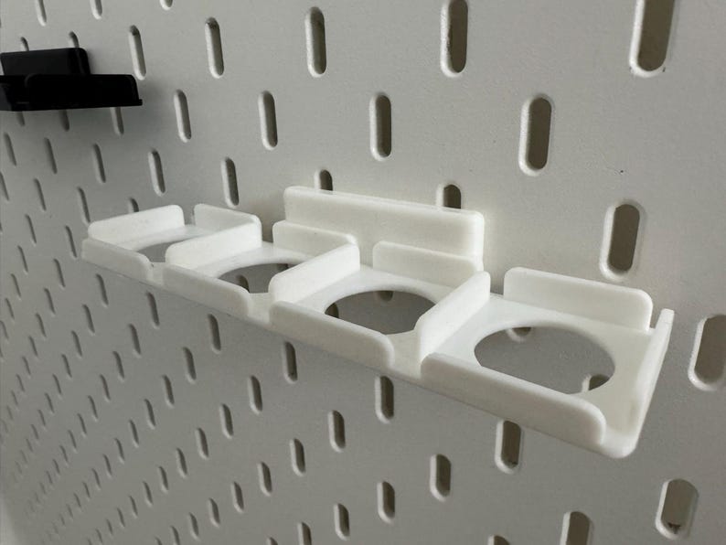 K&ouml;nnte beinhalten: Wei&szlig;e 3D-gedruckte Lochwand-Organizer. Der Haupt-Organizer hat drei kreisf&ouml;rmige &Ouml;ffnungen und ist an einer wei&szlig;en Lochwand befestigt. Ein kleinerer schwarzer Organizer ist ebenfalls an der Lochwand befestigt. Die Lochwand hat gleichm&auml;&szlig;ig verteilte ovale L&ouml;cher.