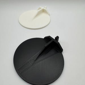 Op de afbeelding: Twee 3D-geprinte ronde schijven met een verhoogd middengedeelte. E&eacute;n schijf is zwart en de andere is wit.