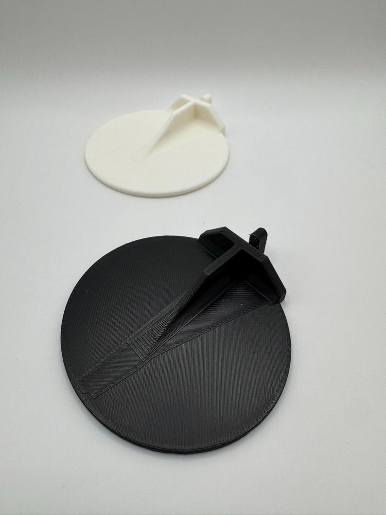 Op de afbeelding: Twee 3D-geprinte ronde schijven met een verhoogd middengedeelte. E&eacute;n schijf is zwart en de andere is wit.