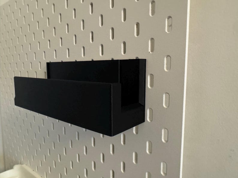 Peut inclure: &Eacute;tag&egrave;re noire rectangulaire fix&eacute;e &agrave; un mur en panneau perfor&eacute; blanc. L'&eacute;tag&egrave;re a un profil en forme de U. Le panneau perfor&eacute; pr&eacute;sente des trous ovales espac&eacute;s. Le mur est de couleur neutre.