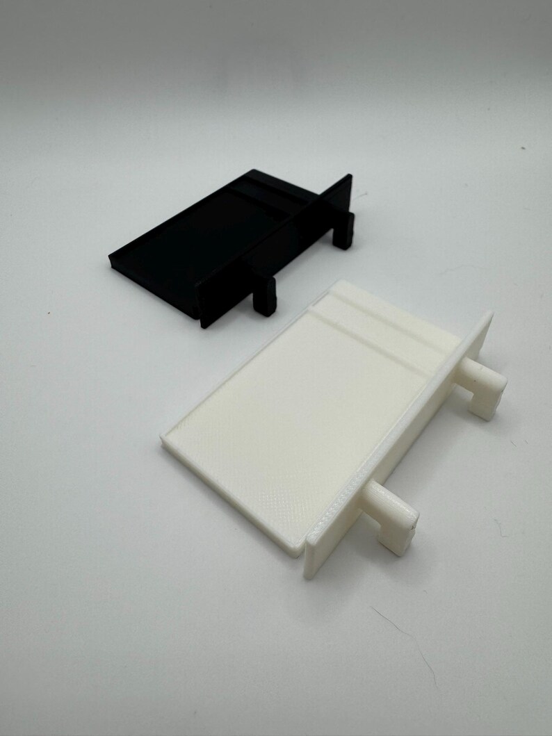 May include: Two plastic shelf brackets, one black and one white. The brackets are rectangular in shape with two small tabs on the side.