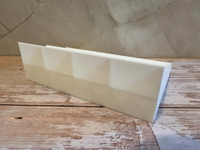 Peut inclure: Un objet rectangulaire en bois de couleur claire avec un dessus inclin&eacute;. L'objet est positionn&eacute; en biais sur une surface en bois. L'arri&egrave;re-plan pr&eacute;sente un mur textur&eacute; de couleur claire.