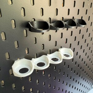 Puede incluir: Un conjunto de seis organizadores de pared de pl&aacute;stico blanco y negro. Los organizadores est&aacute;n dise&ntilde;ados para contener art&iacute;culos peque&ntilde;os como herramientas o accesorios.
