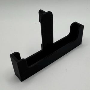 May include: A black plastic phone stand with a vertical support and a horizontal slot for holding a phone.