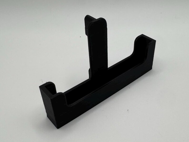 May include: A black plastic phone stand with a vertical support and a horizontal slot for holding a phone.