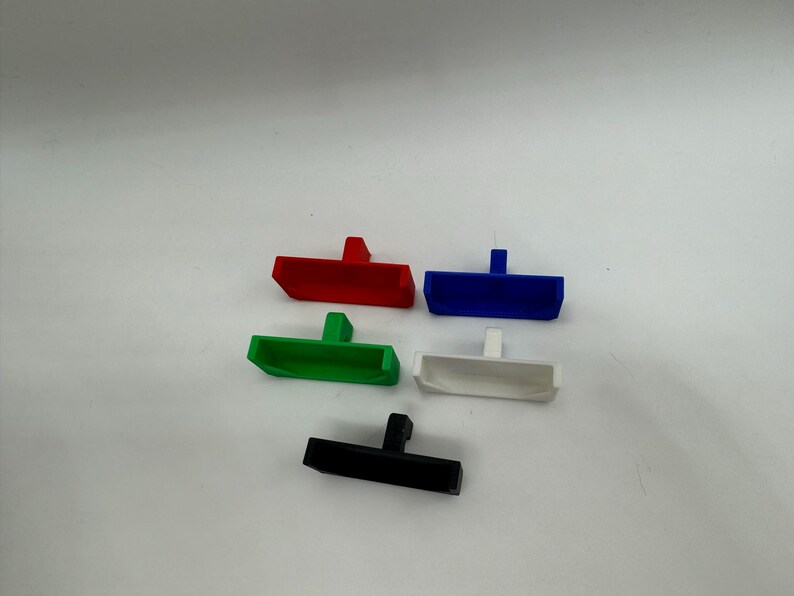 May include: Five plastic drawer pulls in different colours: red, blue, green, white and black. Each pull has a rectangular shape with a small handle on top.