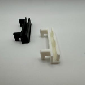 Pode incluir: Duas pe&ccedil;as de pl&aacute;stico, uma preta e outra branca, com um design semelhante. Ambas as pe&ccedil;as t&ecirc;m uma forma retangular com uma borda elevada de um lado e uma ranhura do outro.