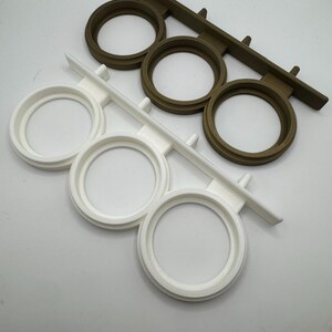 May include: Two sets of three round, white and brown plastic holders for displaying items like candles or small plants. The holders are attached to a rectangular base.