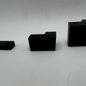 May include: Three black plastic corner brackets of different sizes. The brackets are designed to be used for joining two pieces of wood or other materials at a 90-degree angle.