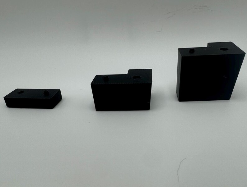 May include: Three black plastic corner brackets of different sizes. The brackets are designed to be used for joining two pieces of wood or other materials at a 90-degree angle.