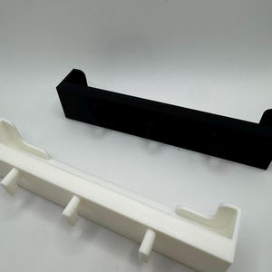 May include: Two rectangular shelves, one black and one white, are displayed against a white background. The white shelf has several small, vertical protrusions. The black shelf is a solid, simple design. Both shelves have a minimalist aesthetic.