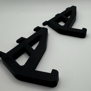 May include: Two black plastic shelf brackets with a triangular shape and a series of holes for mounting.