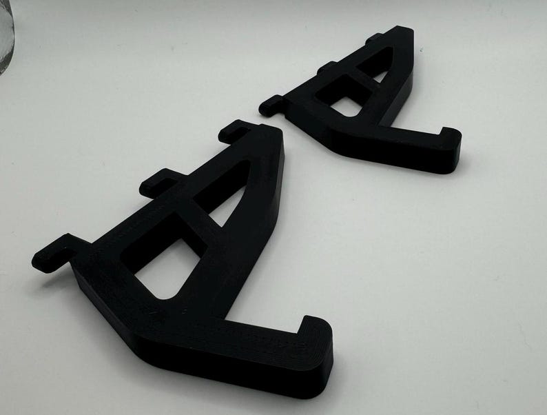 May include: Two black plastic shelf brackets with a triangular shape and a series of holes for mounting.